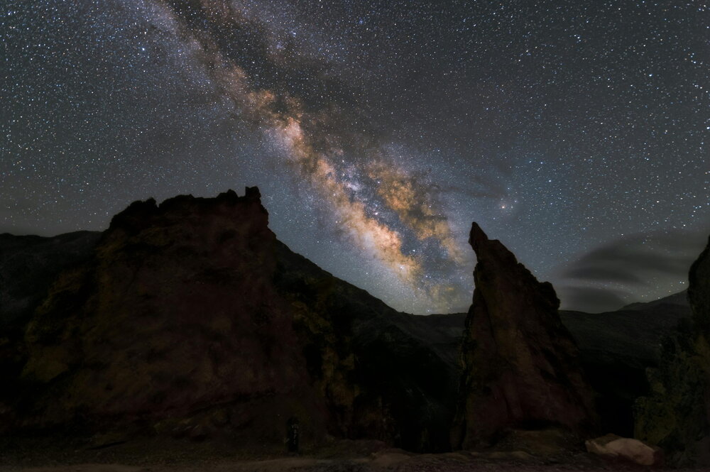 A picture of stars in the sky over a dark rock formation.