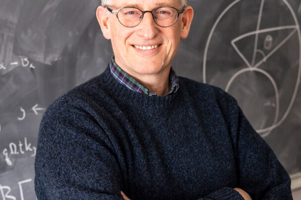 Charles Gammie standing with his arms crossed in front of a chalkboard.