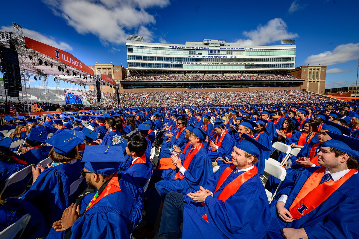 Students sit in their graduation garb in Memorial Stadium.
