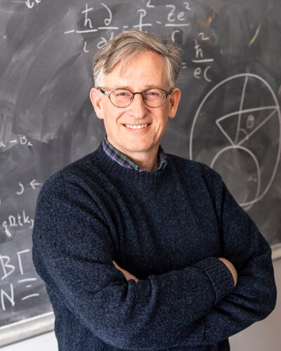 Charles Gammie standing with his arms crossed in front of a chalkboard.
