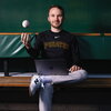 Charlie Young sitting in a dugout with a laptop and tossing a baseball in the air.