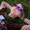 A person laying in the grass with their arms behind their head wearing solar eclipse glasses.