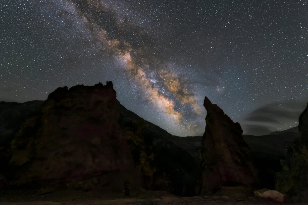 A picture of stars in the sky over a dark rock formation.