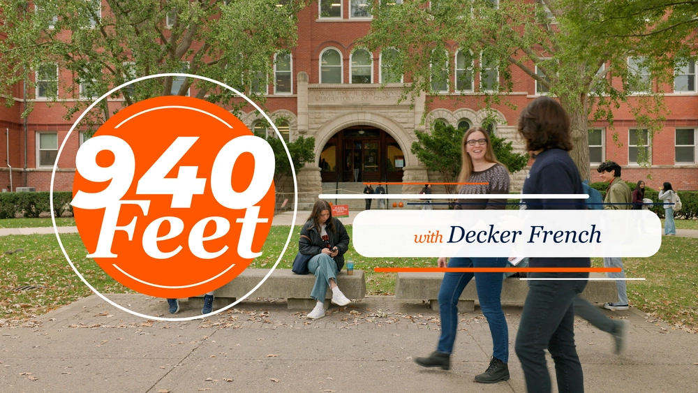 940 Feet with Decker French. Two people walking in front of brick building and people sitting on benches having a conversation.