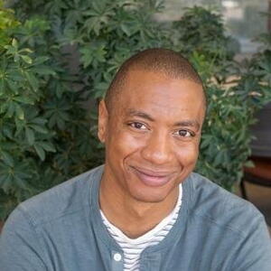 Kirk Barrow, A man in a sweater posing in front of some plants.